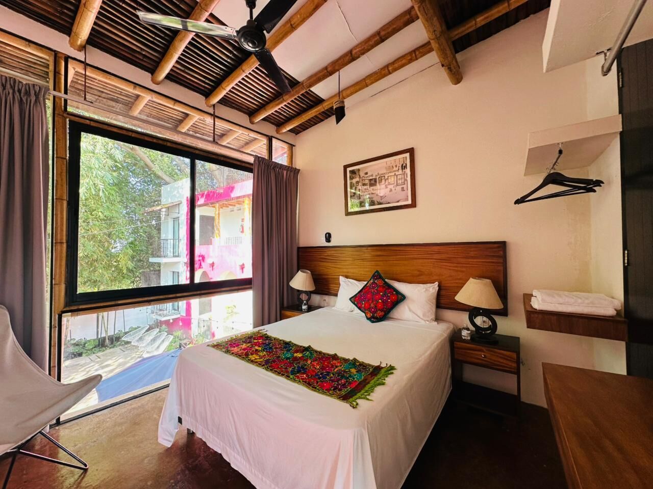 A hotel room with a large bed, two bedside tables, a wooden headboard, a window with curtains, and a view of the outside.