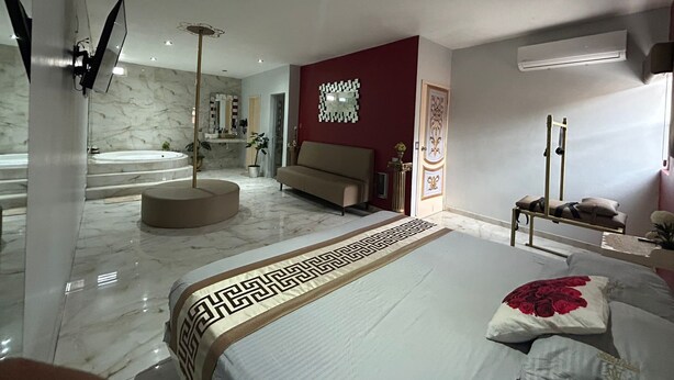A modern bedroom with a large bed, a sitting area, and a bathroom with a bathtub and mirror. - Hotel-Motel Deluxe (Tecuala)