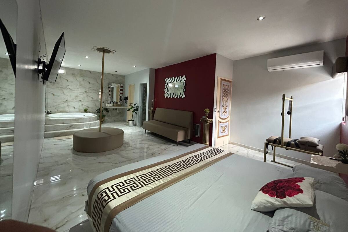 Ein modernes Schlafzimmer mit einem großen Bett, einer Sitzecke und einem Badezimmer mit Badewanne und Spiegel.