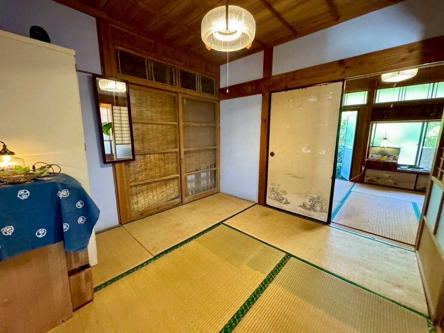 A traditional Japanese room with tatami flooring, sliding doors, and a small table with a blue tablecloth.