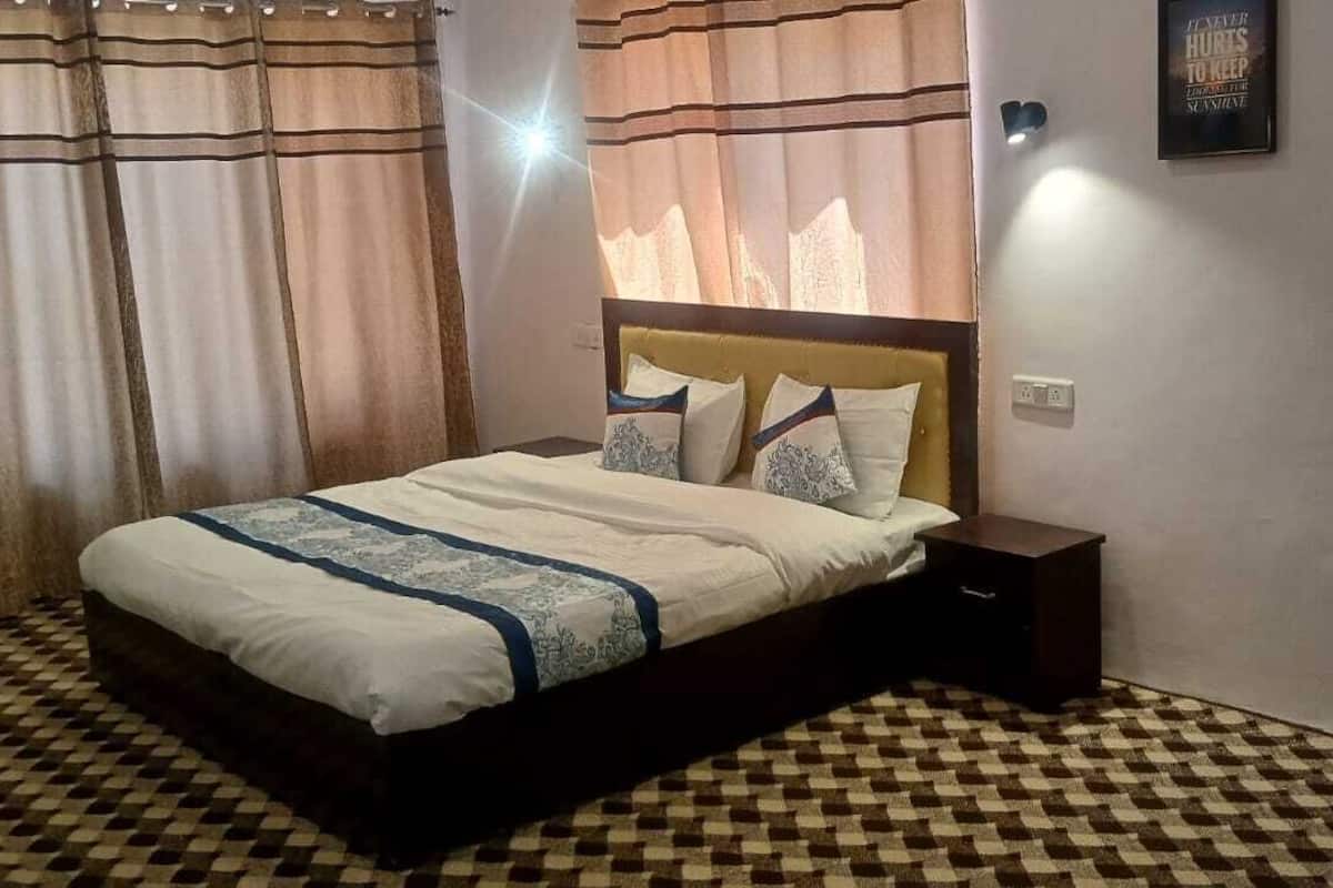 A bedroom with a bed, curtains, a nightstand, and a wall-mounted light.