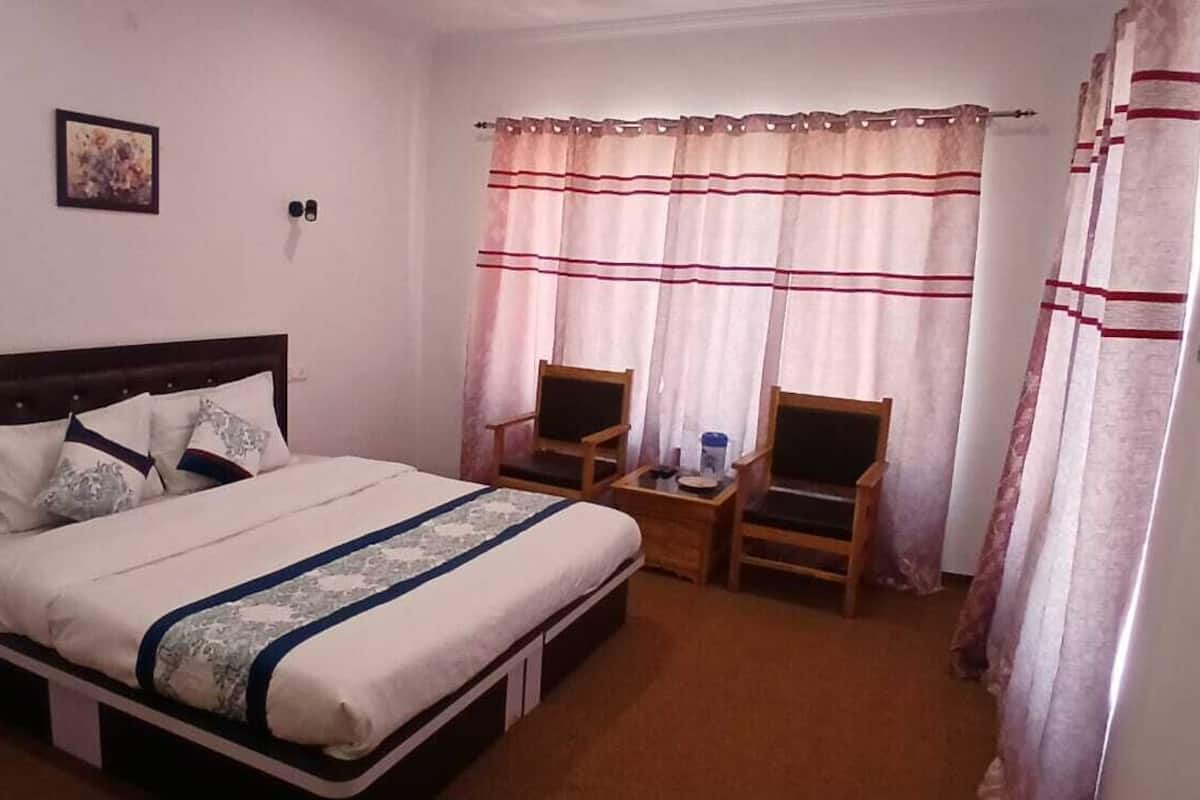 A hotel room with a bed, a small table with two chairs, a nightstand, and a window with curtains.
