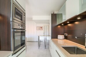 A modern kitchen with built-in appliances, a dining area with a white table and chairs, and a dark wooden accent wall.