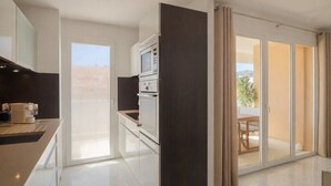 Una cocina moderna con horno y microondas integrados, una puerta corrediza de vidrio que da a un balcón con mesa y sillas, y vistas al exterior.