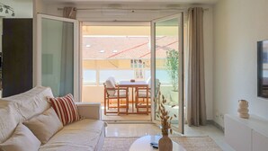Una sala de estar moderna con un sofá, una mesa de centro y un ventanal corredizo que da a un balcón exterior con un comedor.