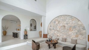 A modern living room with a stone accent wall, a sofa, a coffee table, and a seating area with a patterned rug. - 3BR Rooftop Summary: (Kabupaten Badung)