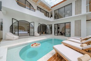 A modern indoor pool area with lounge chairs and a floating bar. - 3BR Rooftop Summary: (Kabupaten Badung)