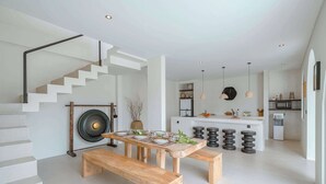 A modern kitchen with a central island, wooden stools, and a dining table set for four. - 3BR Rooftop Summary: (Kabupaten Badung)