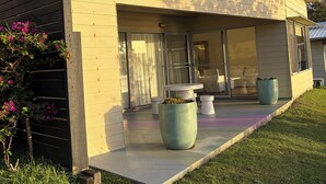 A modern house with a patio area, large planters, and a grassy lawn. - Yallumbee, Seal Rocks - Modern, Private Beach House In Prime Location (Seal Rocks)