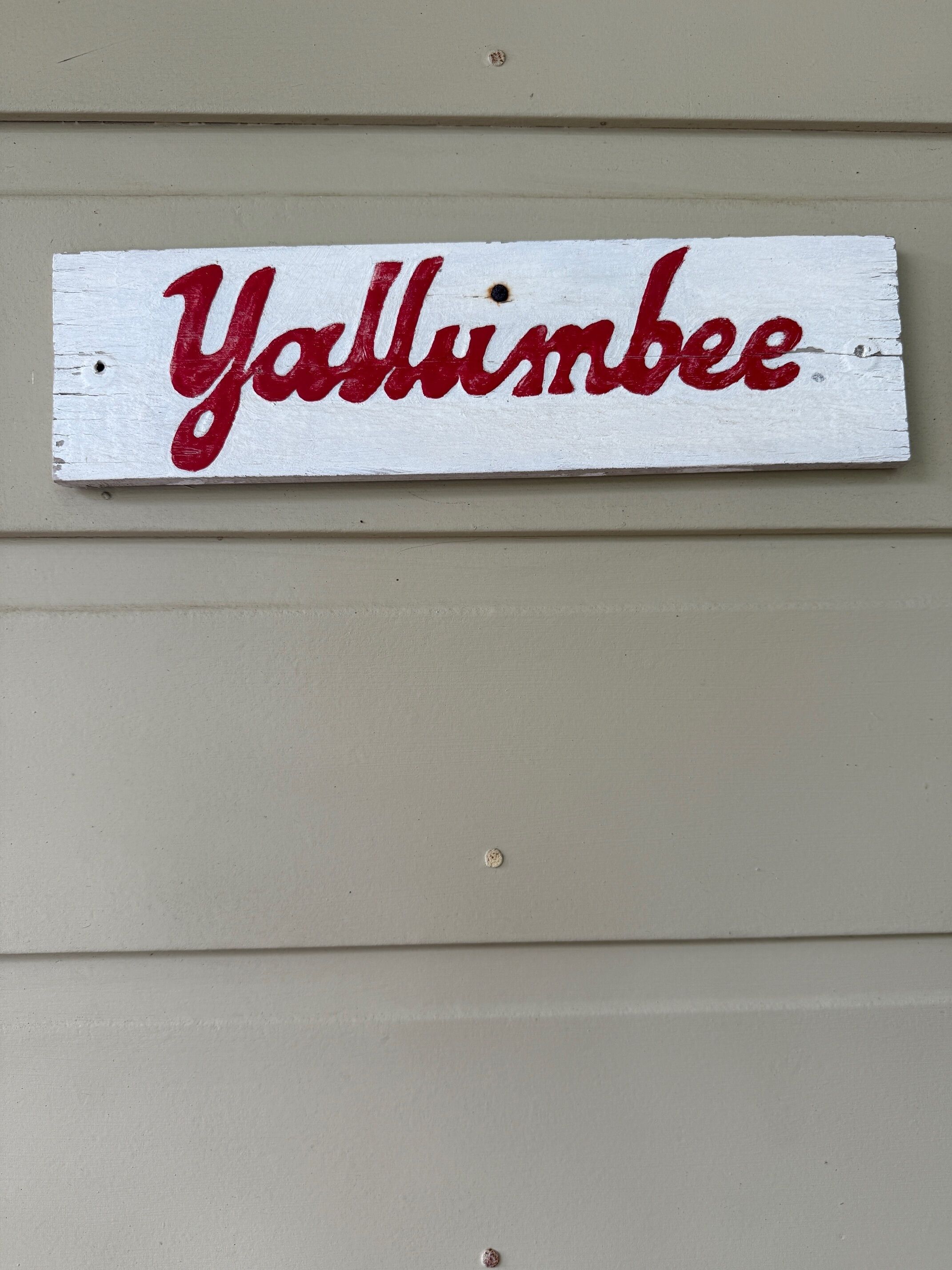 A wooden sign with the text "Y'allumbee" painted in red.