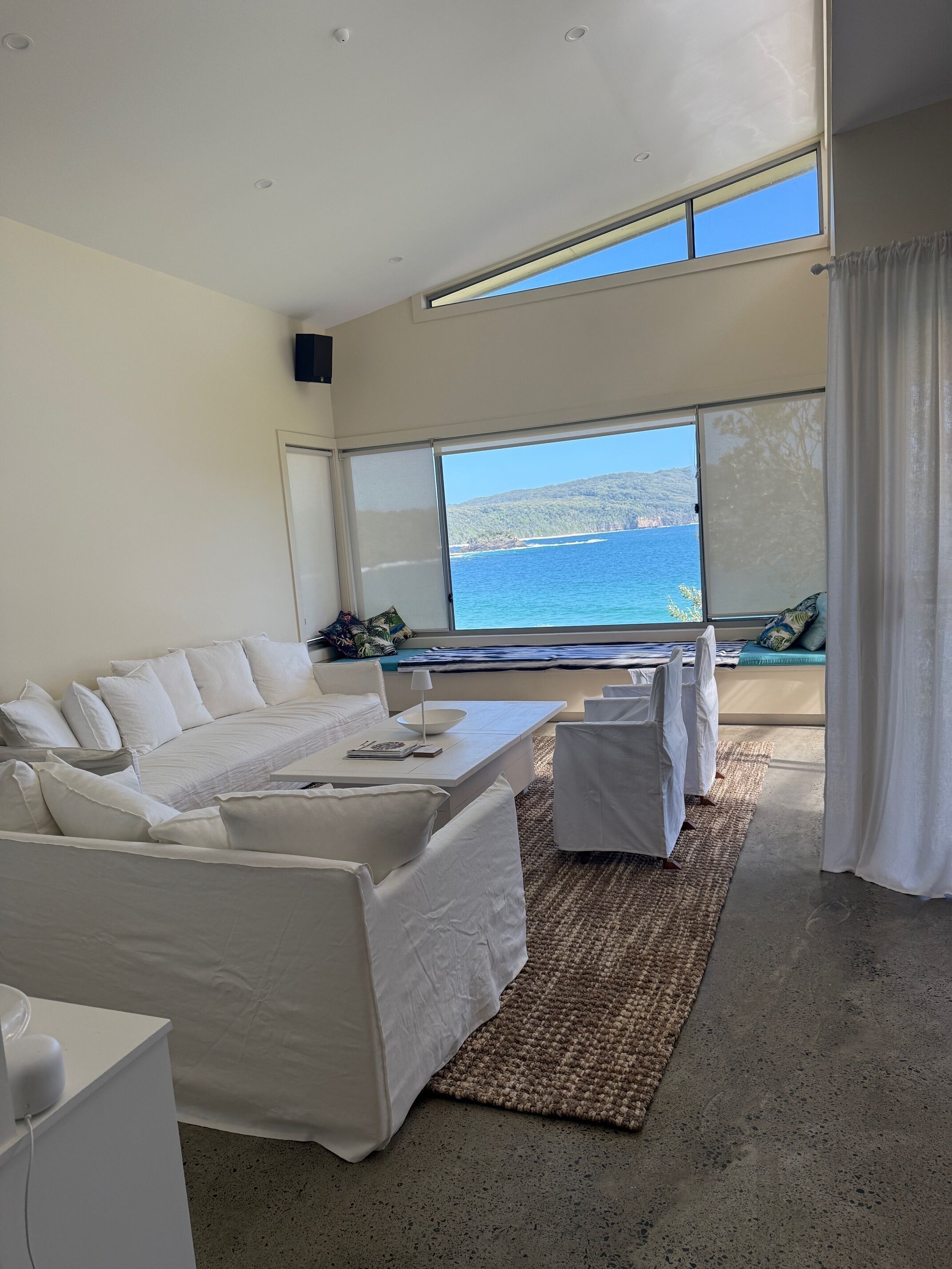 A modern living room with a large window offering a view of the sea and hills.
