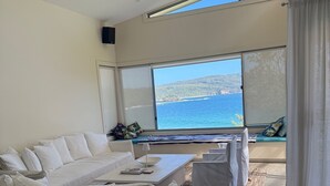 A modern living room with a large window offering a view of the sea and hills. - Yallumbee, Seal Rocks - Modern, Private Beach House In Prime Location (Seal Rocks)