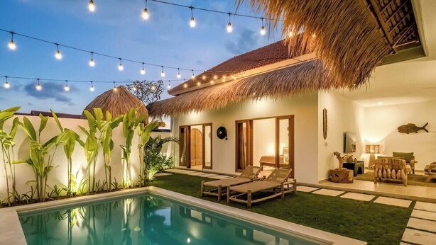Un espace aménagé au bord de la piscine, avec une structure à toit de chaume, des chaises longues et des guirlandes lumineuses.