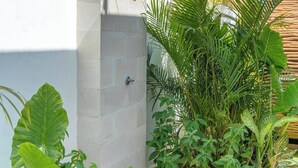Un espace de douche extérieur moderne, doté d’une terrasse en bois et entouré d’une végétation tropicale luxuriante.