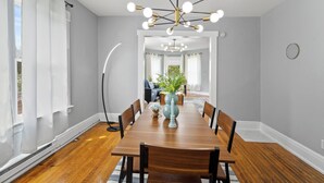 A dining room with a wooden table, chairs, a vase with flowers, and a modern chandelier. - Spacious 2BR Near Syracuse Uni, Zoo & Downtown (Syracuse)