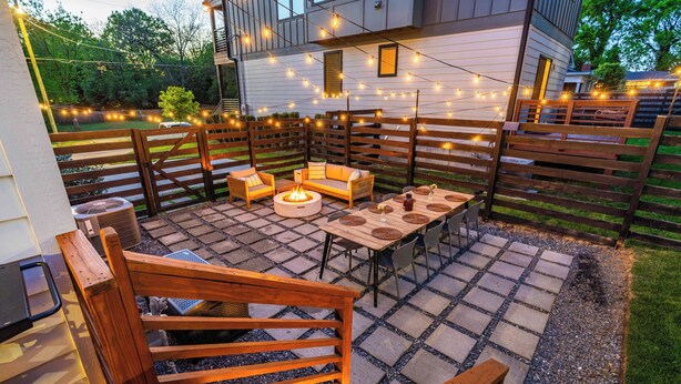 Un patio al aire libre con una chimenea, muebles de madera y luces colgantes.