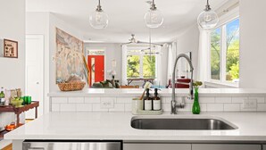 Una cocina moderna con armarios blancos, un lavamanos de acero inoxidable y lámparas colgantes.