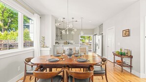 Un comedor con una mesa de madera, seis sillas y una araña. Se ve un ventanal con vistas a zonas verdes.