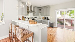 Una cocina moderna con una isla central, armarios blancos y una zona de comedor con sillas de mimbre.