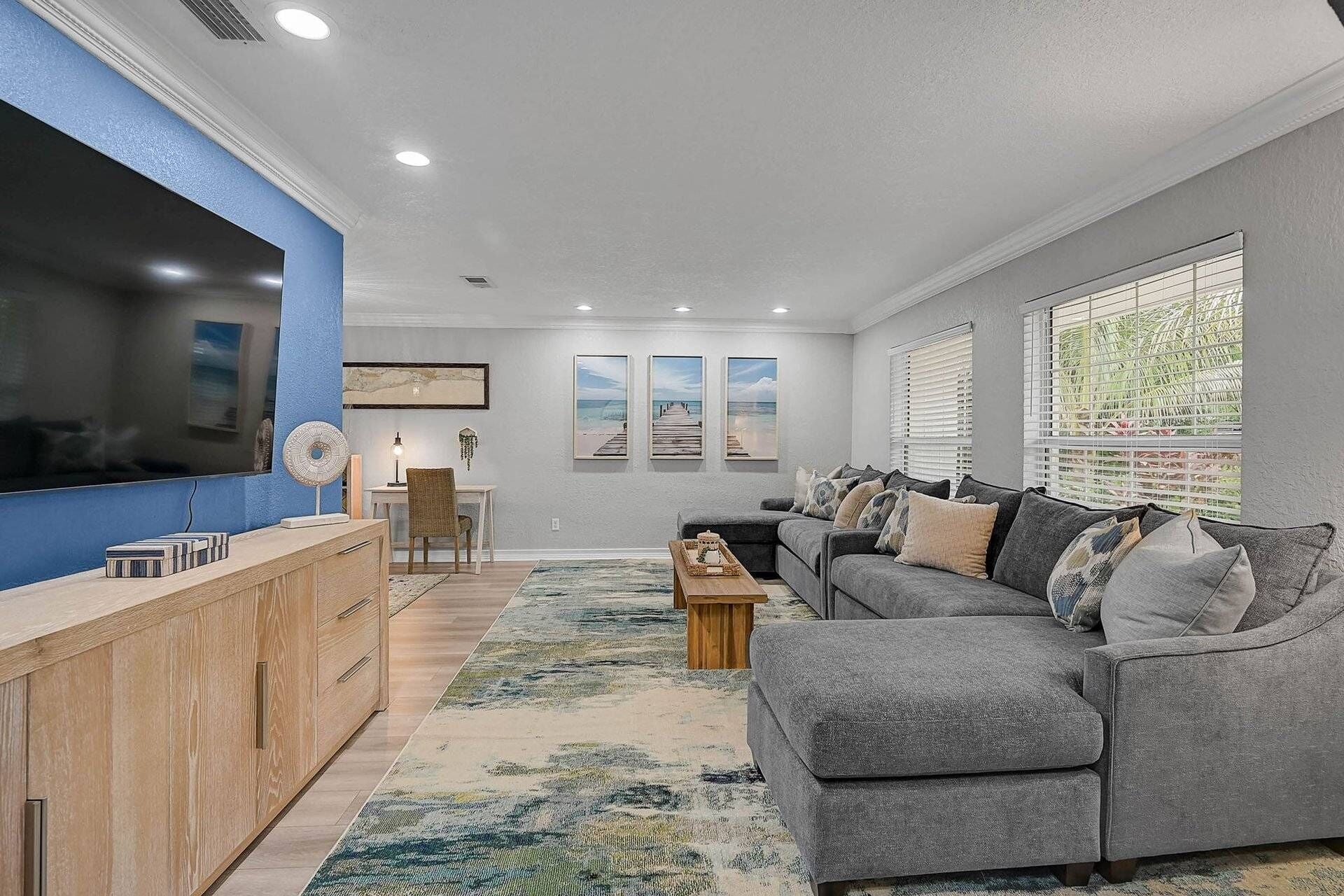 A modern living room with a grey sofa, a wooden coffee table, and a TV on a blue wall.