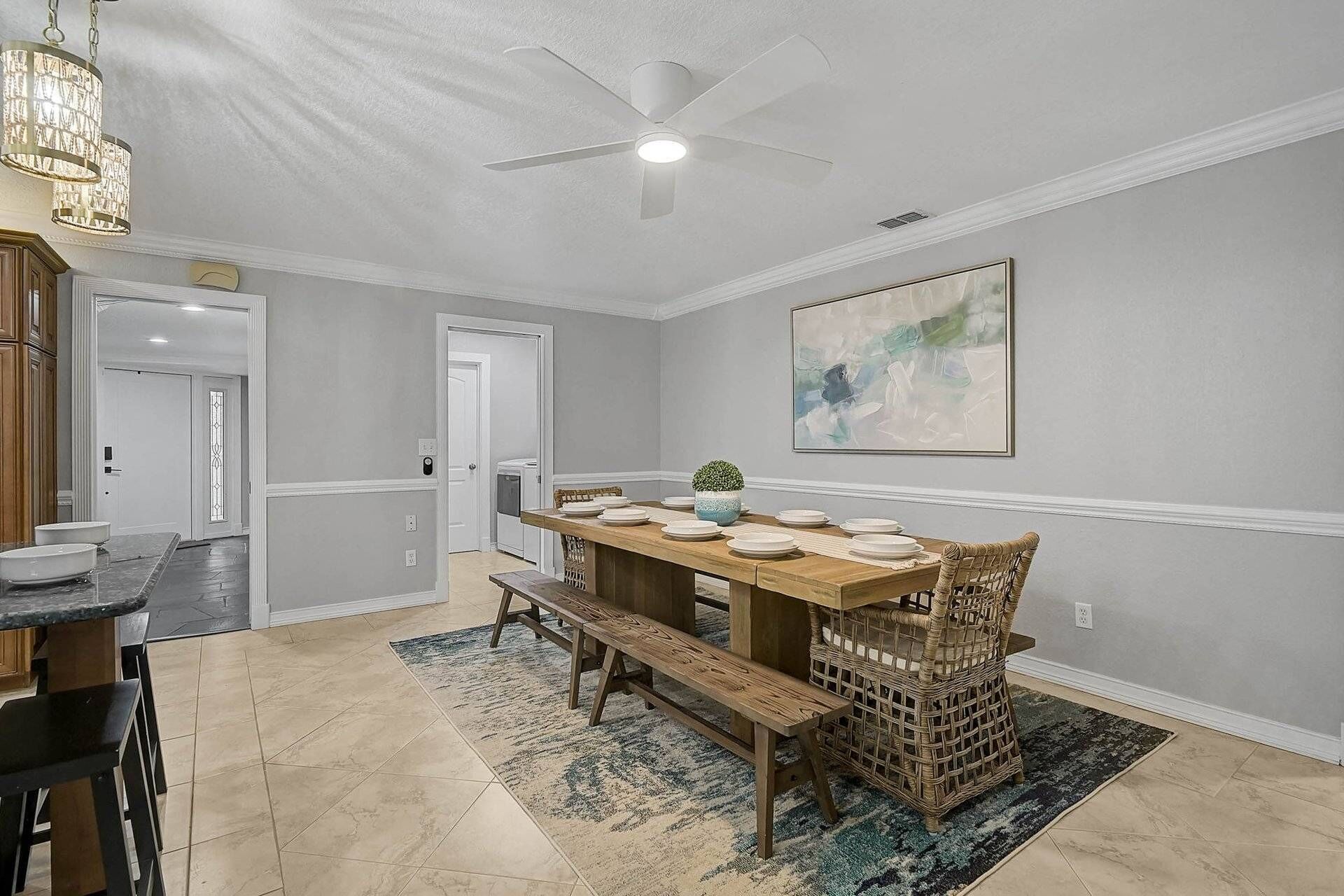 A dining area with a wooden table set for four, a ceiling fan, and a large abstract painting on the wall.