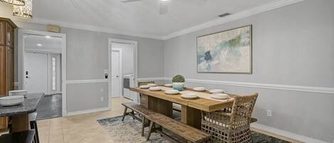 A dining area with a wooden table set for four, a ceiling fan, and a large abstract painting on the wall.
