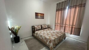 Un dormitorio con una cama, una mesita de noche, un cuadro, una planta en maceta y una ventana con cortinas.