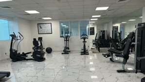 Un gimnasio con diferentes equipos de ejercicio, un espejo grande y suelo de baldosas.