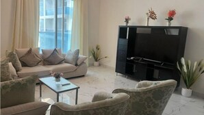 Un salón con sofá, sillones, una mesa de centro, un mueble para televisión con televisor de pantalla plana y plantas en macetas.
