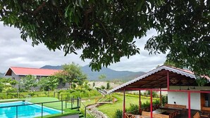 A pool with a wooden deck, a covered seating area, and a view of a mountain in the background.