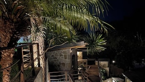 A nighttime pathway leading to a stone building with a wooden railing and palm trees.