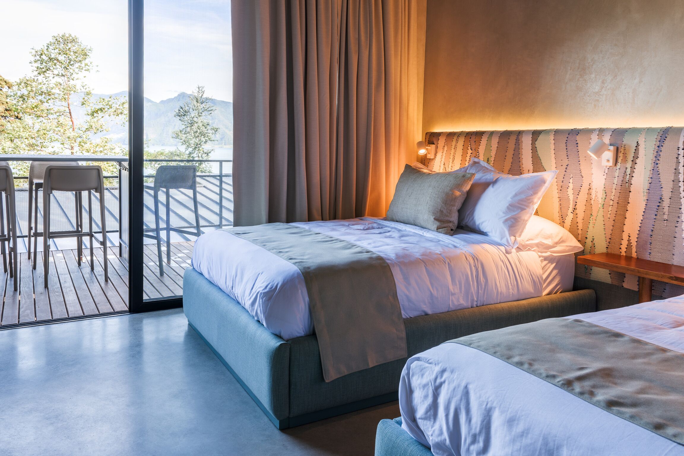 Une chambre avec un grand lit, un plus petit lit, un balcon avec des chaises et une vue sur les montagnes.