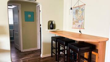A kitchen with a wooden bar and stools, a 'WELCOME FRIENDS' sign, a map on the wall, and a door leading to another room.
