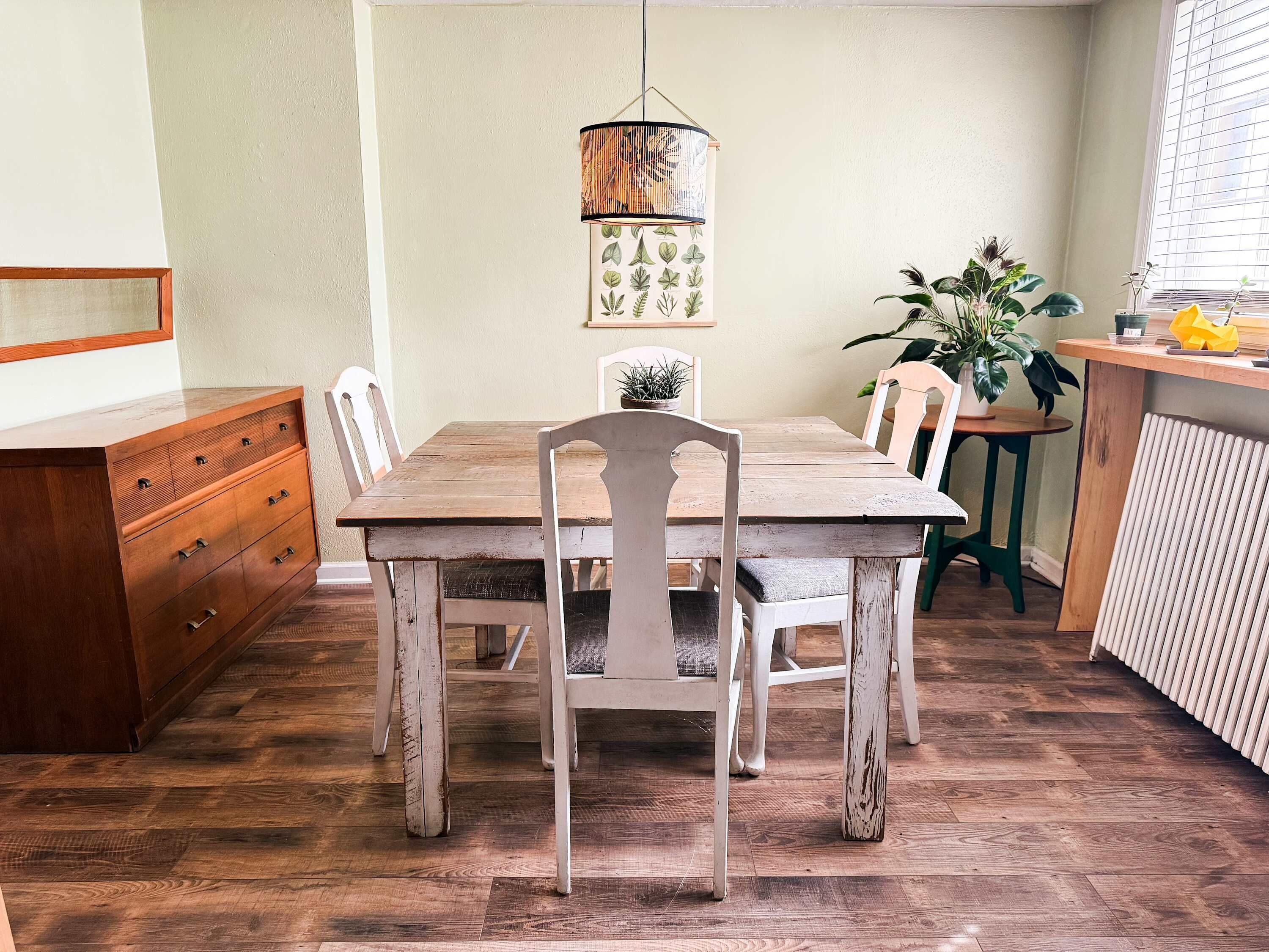 A dining area with a wooden table and chairs, a hanging light fixture, and a potted plant.