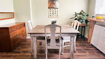 A dining area with a wooden table and chairs, a hanging light fixture, and a potted plant.