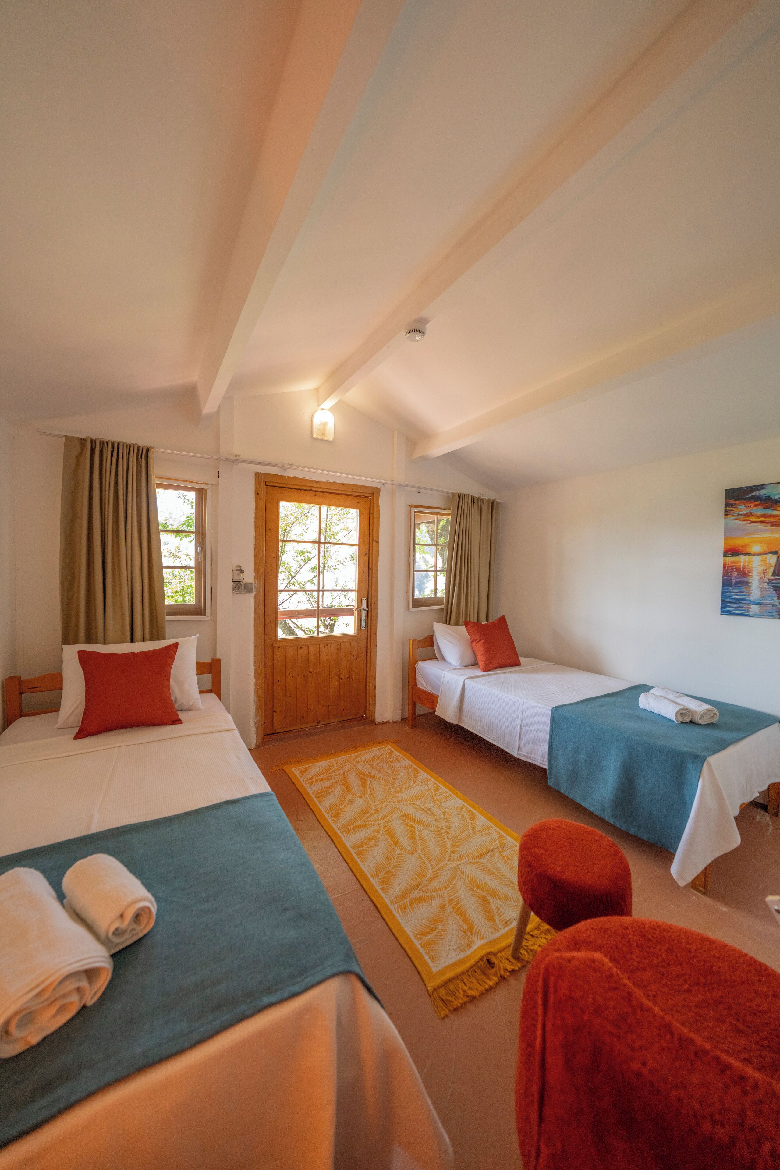 A room with two beds, a wooden door, a window, and a painting on the wall.