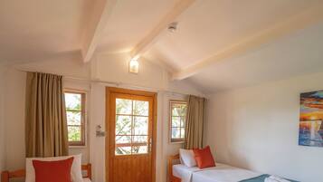 A room with two beds, a wooden door, a window, and a painting on the wall.