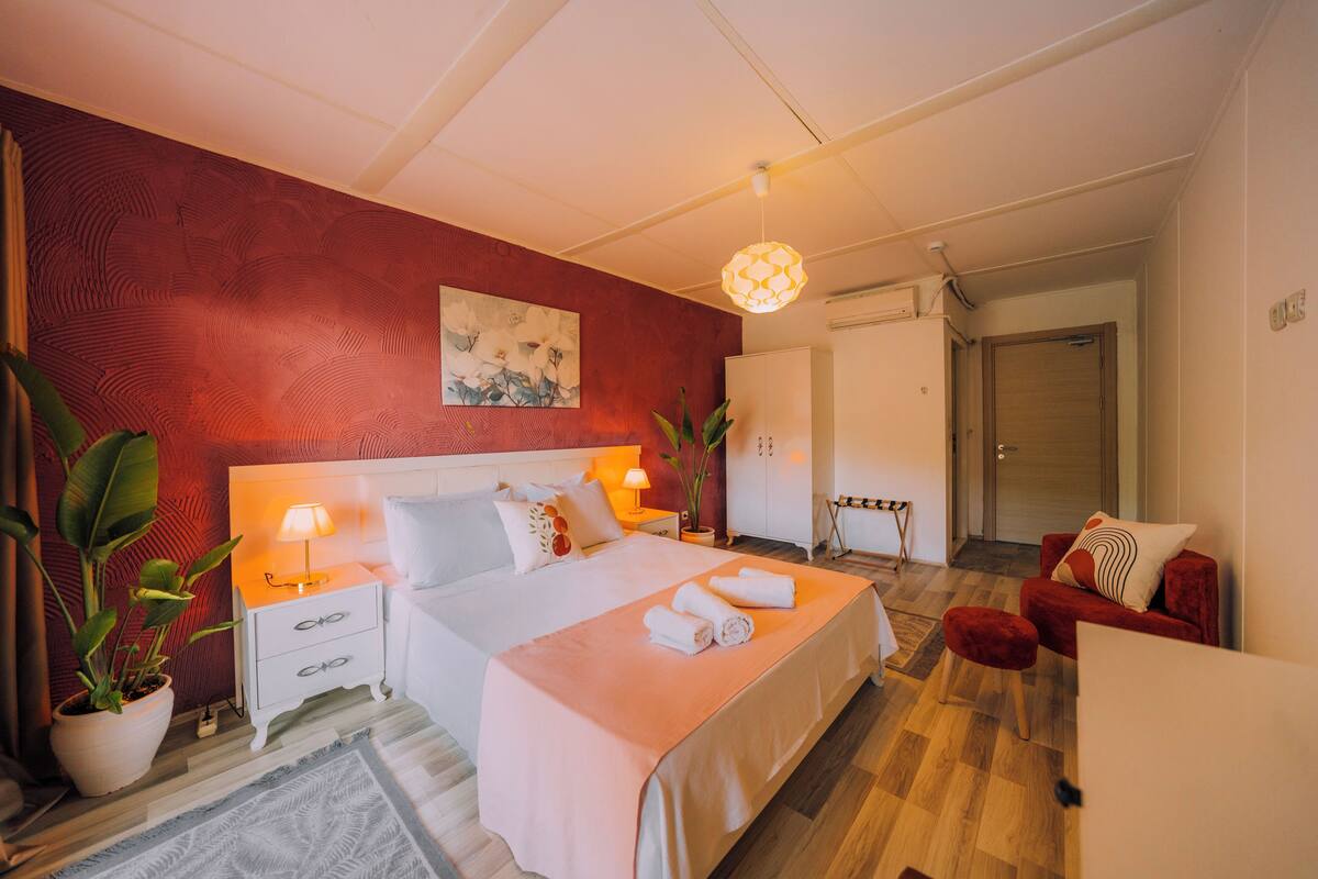 Une chambre à coucher moderne avec un lit, des tables de chevet, une petite table, une plante en pot et une chaise rouge.