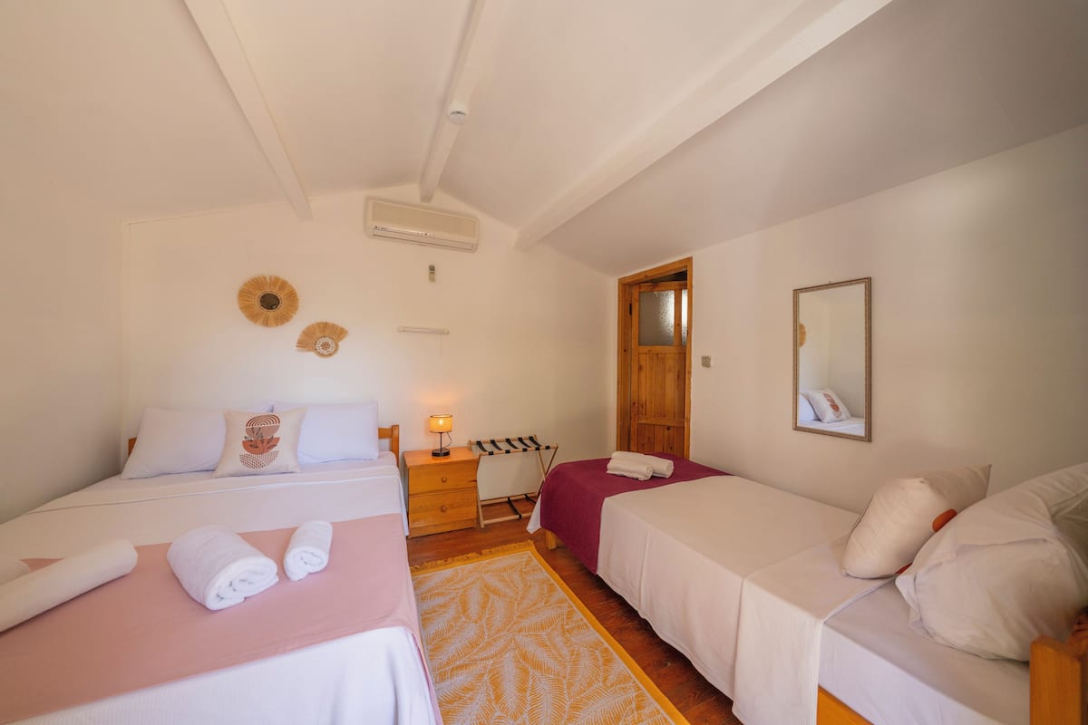 Une chambre d’hôtel avec deux lits, une table de chevet en bois, un miroir et une porte donnant sur une autre pièce.