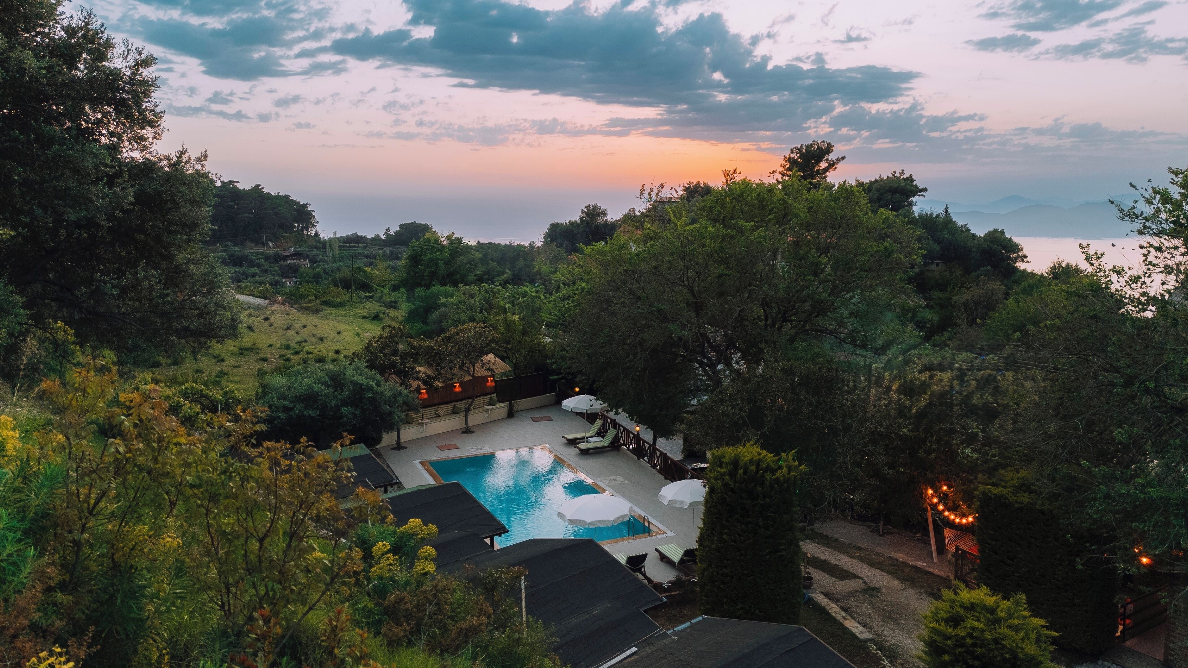 Uma área de piscina com espreguiçadeiras e guarda-sóis, cercada por árvores e colinas.