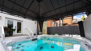 A hot tub under a covered patio with a wooden fence and a house in the background.