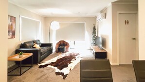 A living room with a leather sofa, a small table, a cowhide rug, a floor lamp, a Christmas tree, and a TV stand. - Canvas of Comfort — A Modern Townhouse of Four Suites (Hamilton)