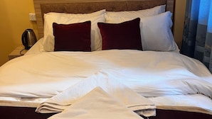 A hotel room with a bed, pillows, a nightstand, a lamp, and a wall socket. - Jhigu Chhen Homestay and Nepal (Bhaktapur)
