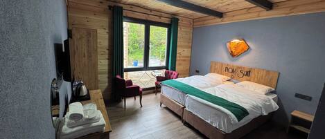A room with a wooden ceiling, a bed with a 'nav suit' headboard, a desk with a kettle, and a view of greenery outside.