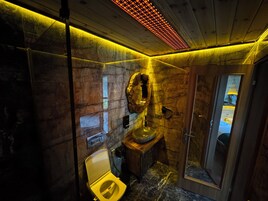 Un baño moderno con pared de mármol, tocador de madera, cabina de ducha de vidrio y inodoro amarillo.