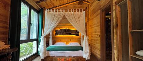Un dormitorio de cabaña de madera con cama con dosel, un ventanal grande y techo rústico.