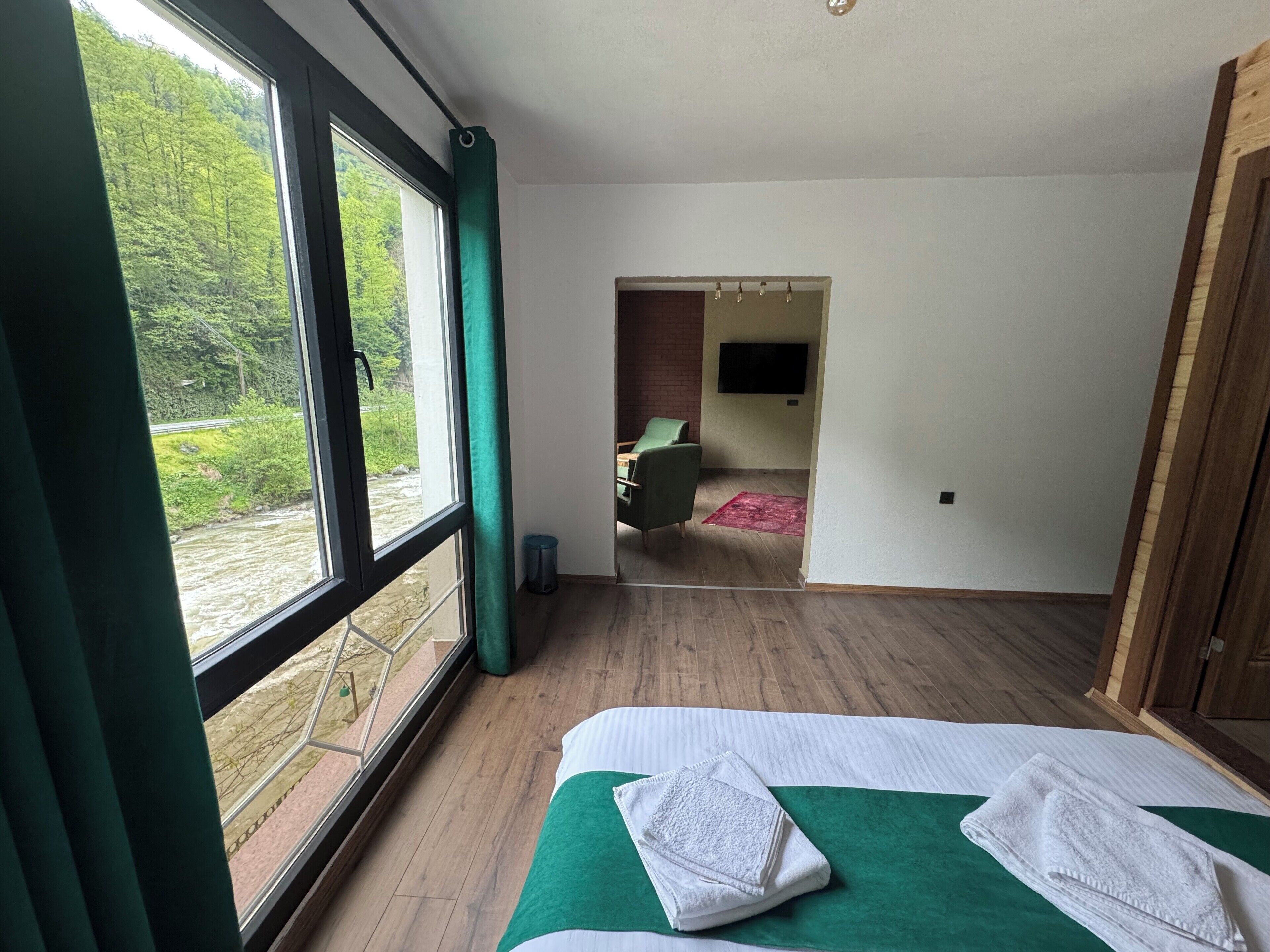 A bedroom with a large window, a bed with a green and white bedspread, and a view of a forested area.