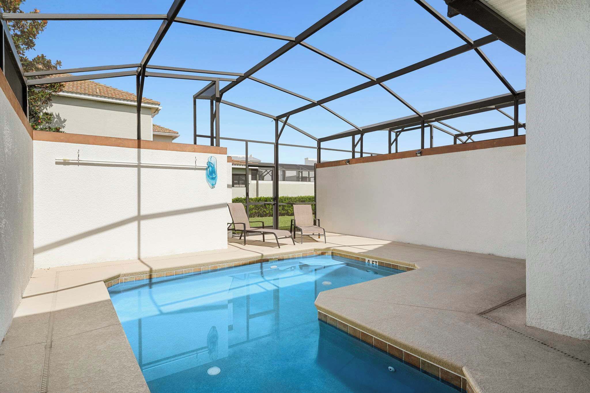 Piscina ao ar livre coberta por um teto de vidro, cercada por espreguiçadeiras e uma parede branca.