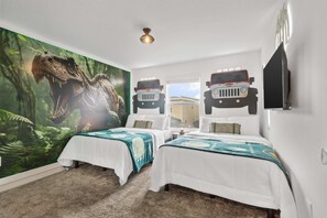 Une chambre avec deux lits, une grande fresque représentant un dinosaure et un autocollant représentant un camping-car Jeep sur le mur.