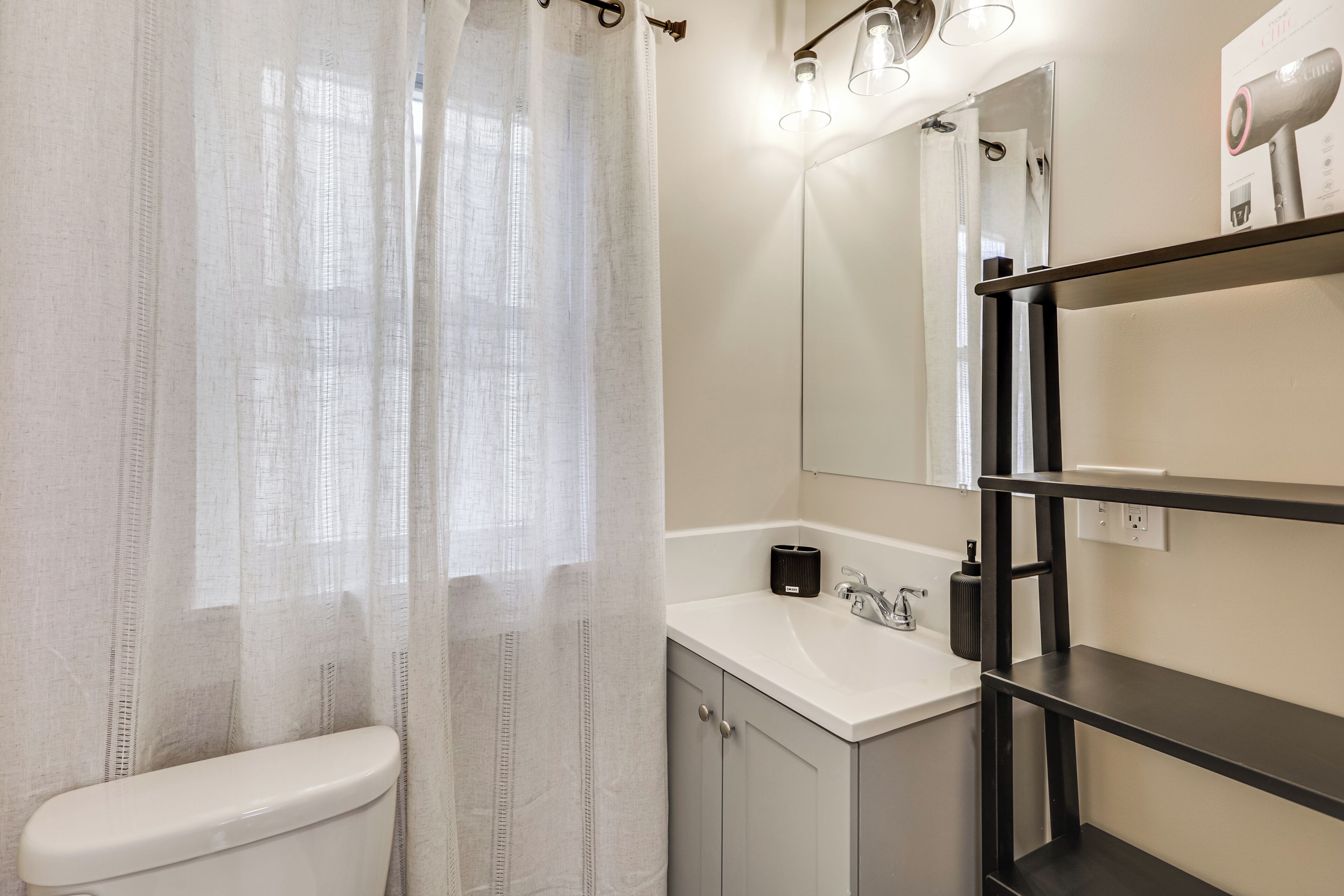 Une salle de bain équipée de toilettes, d’un lavabo, d’un miroir et d’une étagère.